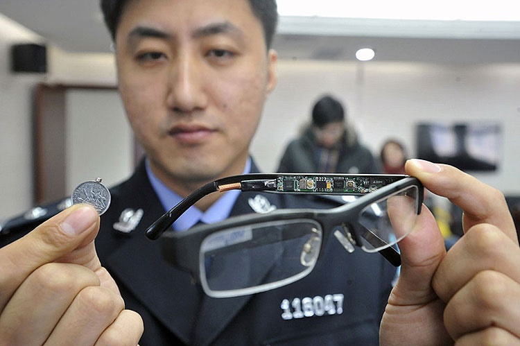 A police officer displays a pair of glasses with a hidden camera and a tiny receiver attached to a coin, equipment used to cheat on exams, confiscated by the police in Shenyang, Liaoning province, China