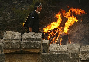 A firefighter passes next ancient pieces of columns as the fire burns at Olympia