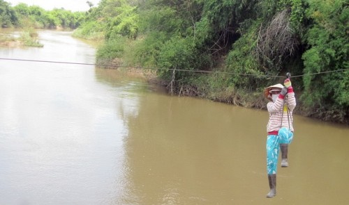 A woman is seen using a homemade suspended cable system with a pulley to cross the Krong Ana River i